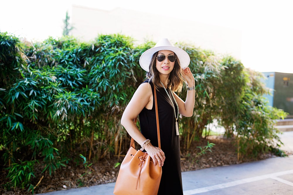 mommy blogger in black sleevless midi dress and mansur gavriel bucket bag