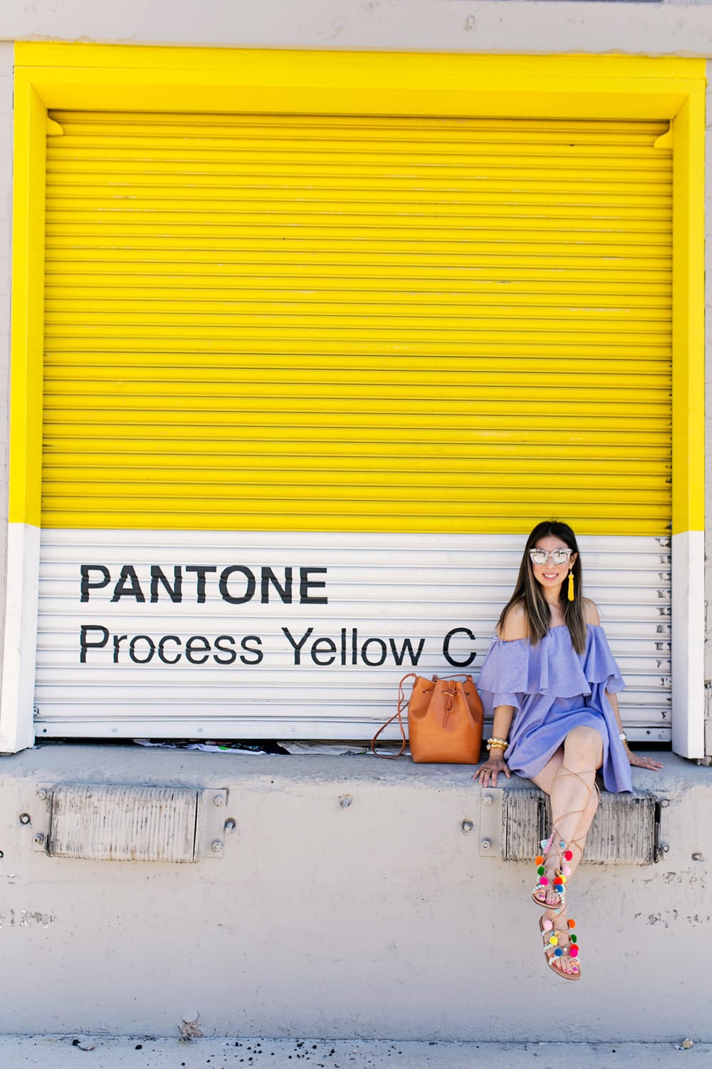 off the shoulder dress with pom pom sandals in front of yellow wall