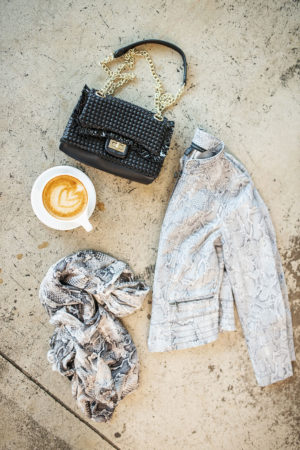 flatlay of whbm snake print moto jacket, sequin scarf, coffee, and woven bag